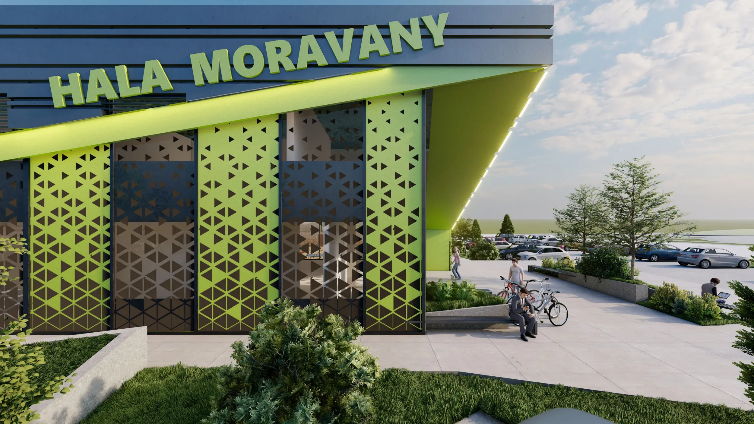 Boční pohled z parkovacích míst na halu. Je zde vidět částečně prosklená fasáda, velký šikmý nápis "Hala Moravany" a také trojúhelníkové tvary nakreslené na fasádu haly zelenou nebo šedivou barvou. 